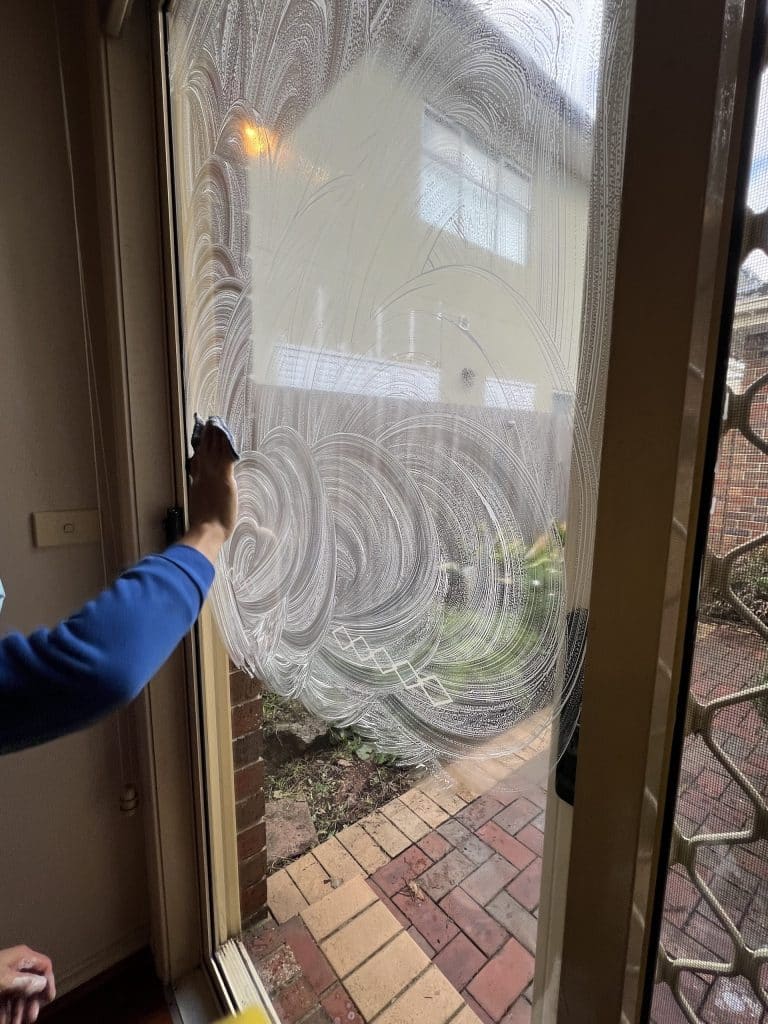 O2OCleaning cleaner washing a large window with soapy water, creating circular patterns on the glass.