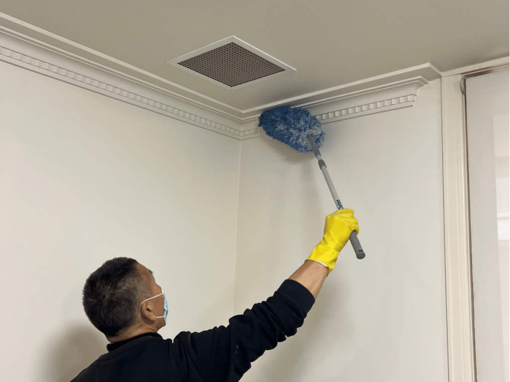 A cleaning professional using a duster to clean a ceiling corner.