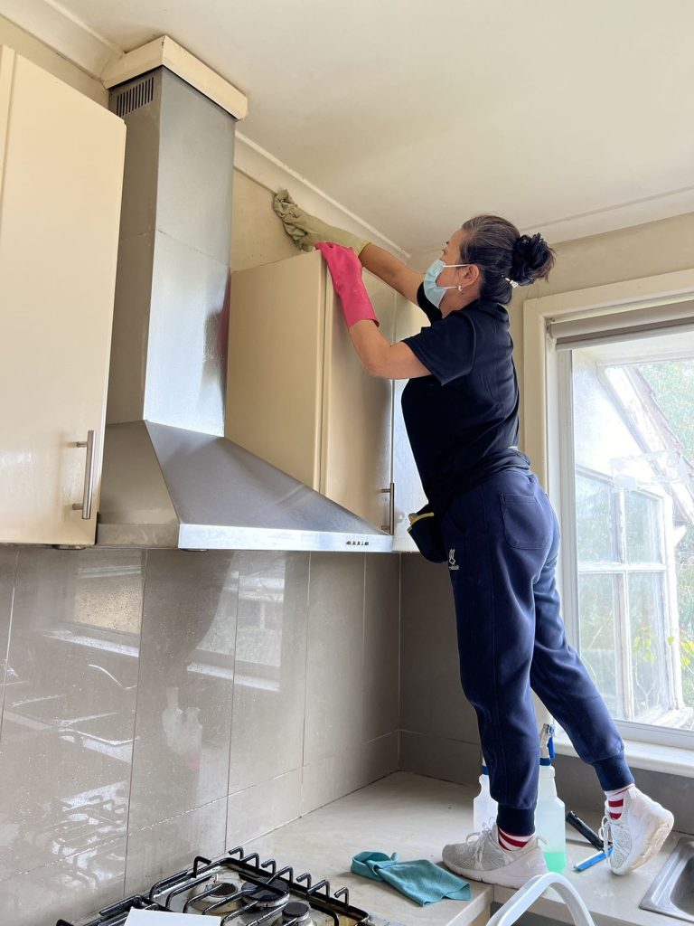 Cleaning professional dusting a high window inside a rental property.