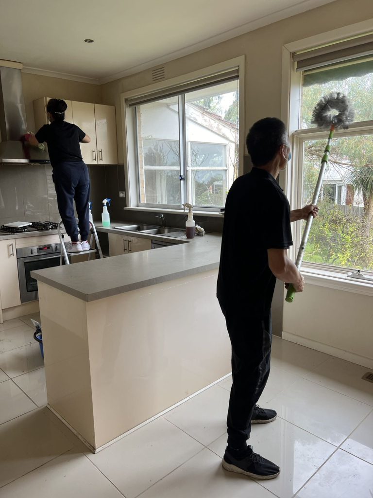 Professional cleaner wiping down the top of a kitchen cabinet next to a range hood.