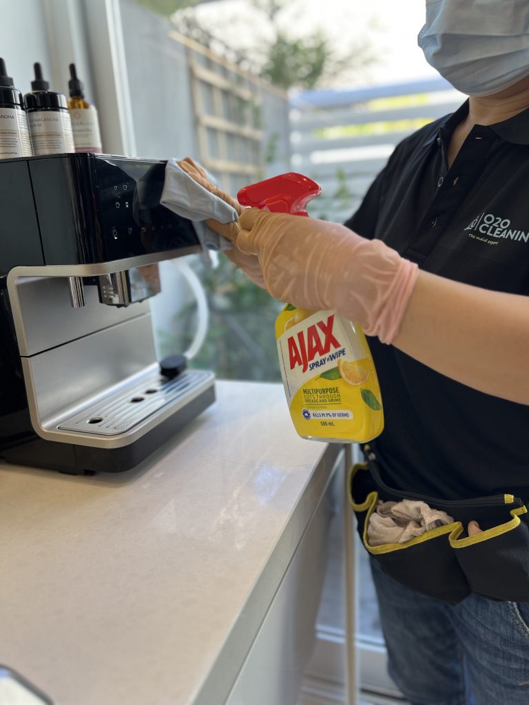 A professional cleaner using an Ajax multipurpose cleaner to wipe down a kitchen appliance.