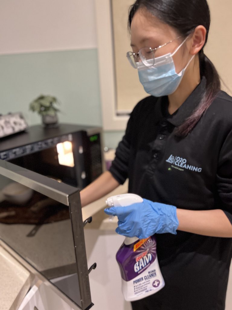 House cleaner in Melbourne using a cleaning solution to disinfect a microwave